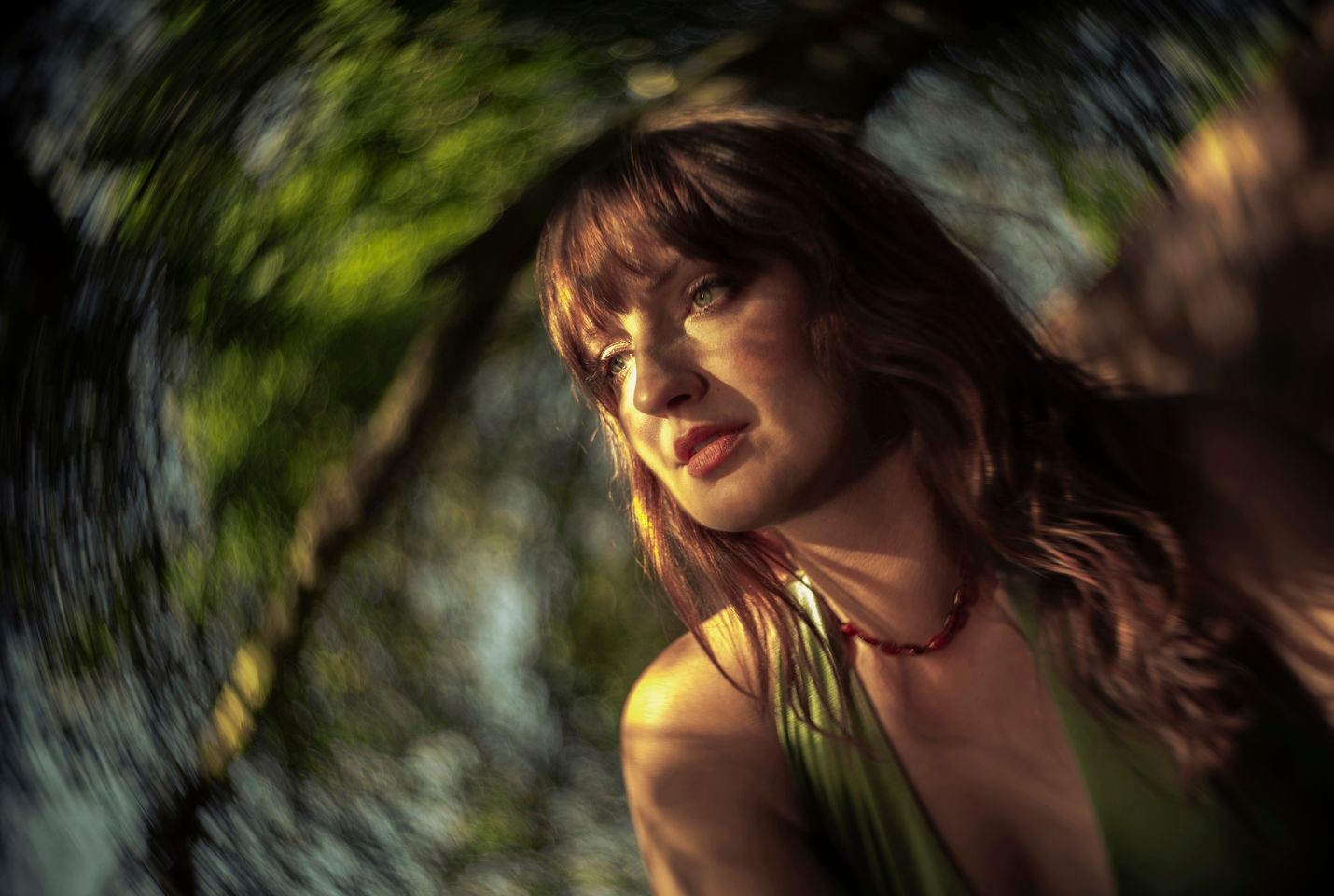 A close up image of a woman with wavy brown hair wearing a red necklace and green top